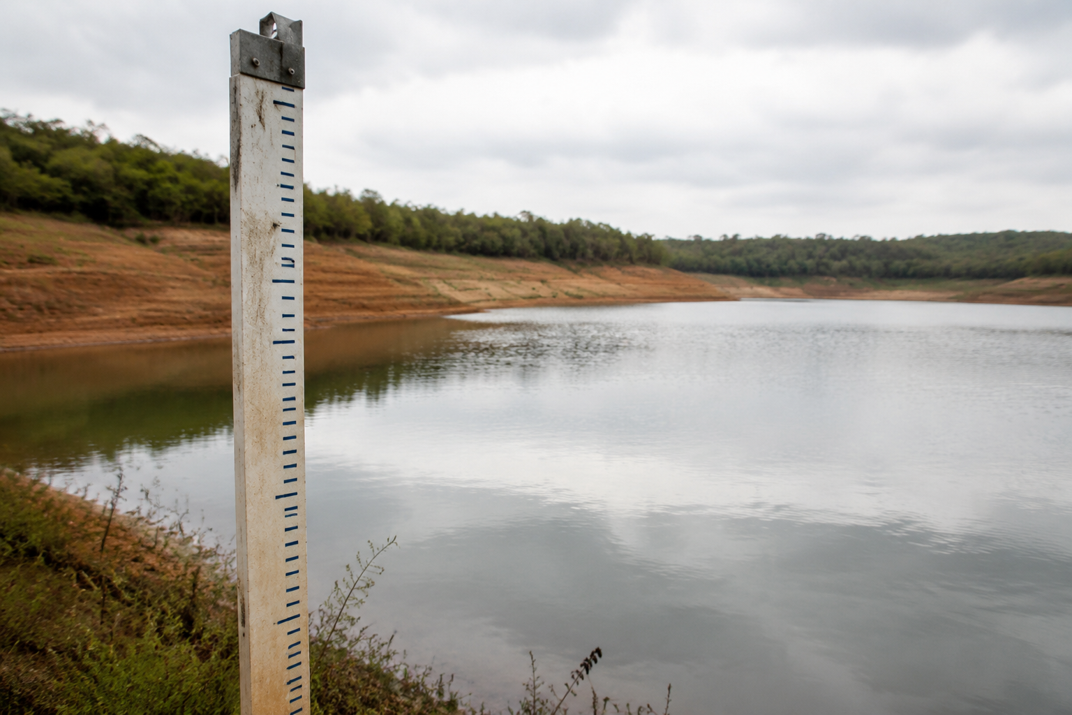 Régua de monitoramento diante de reservatório com faixa de solo exposta nas margens